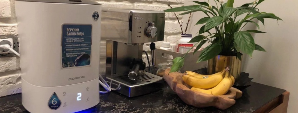 Увлажнитель Polaris PUH 7005 TFD стоит на кухонной столешнице рядом с кофеваркой, бананами и цветком в горшке
